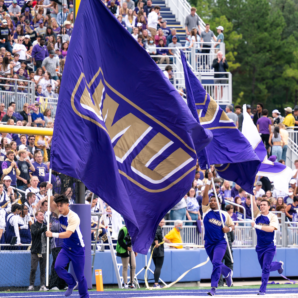 JMU Spirit Leaders running in front of crowd with field runner flag